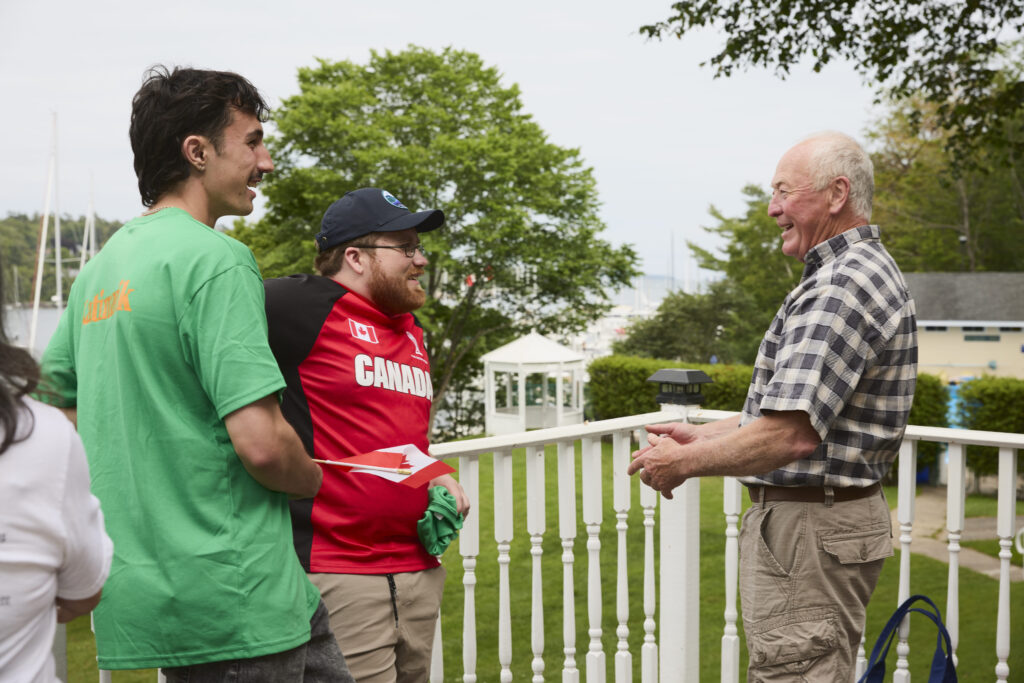 Intergenerational conversation between young Katimavik participants and a community member on an outdoor deck.